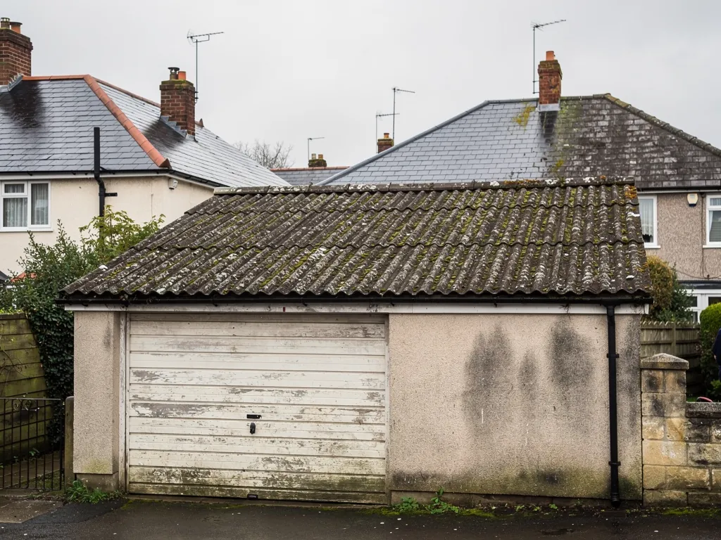 A detached garage with a corrugated cement-sheet roof showing age and lichen