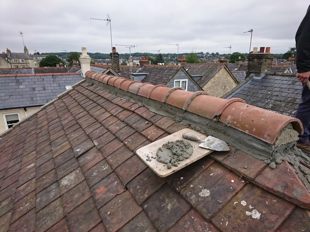 Half-round ridge tiles being re-bedded on a tiled roof